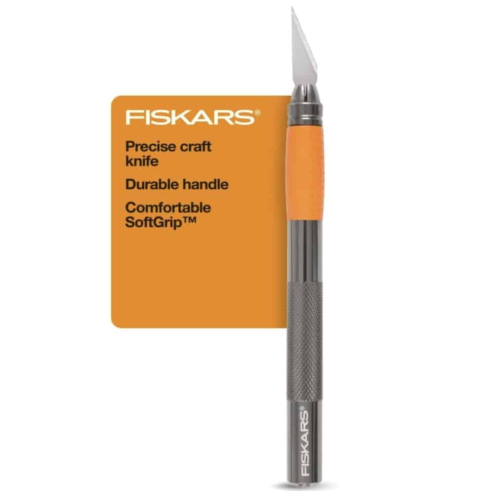 A Fiskars precise craft knife with a silver blade, gray handle, and orange SoftGrip™ section—perfect for creating easy corkboard placemats. Text beside it highlights the tool's precision, durable handle, and comfortable grip.